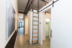 A modern interior with a central staircase, a hallway with artwork, and a door leading to another room.