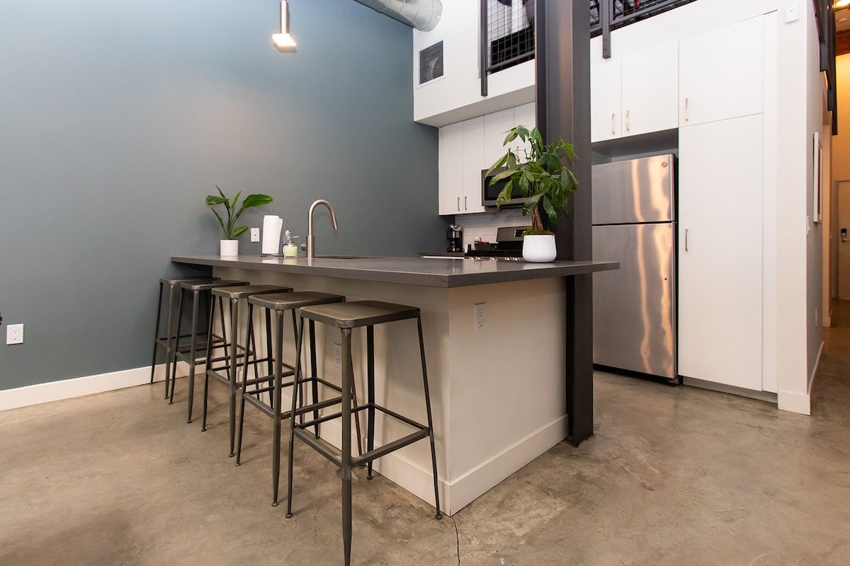 A modern kitchen with a bar area, white cabinets, stainless steel appliances, and a grey wall.