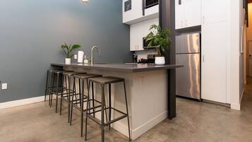 A modern kitchen with a bar area, white cabinets, stainless steel appliances, and a grey wall.