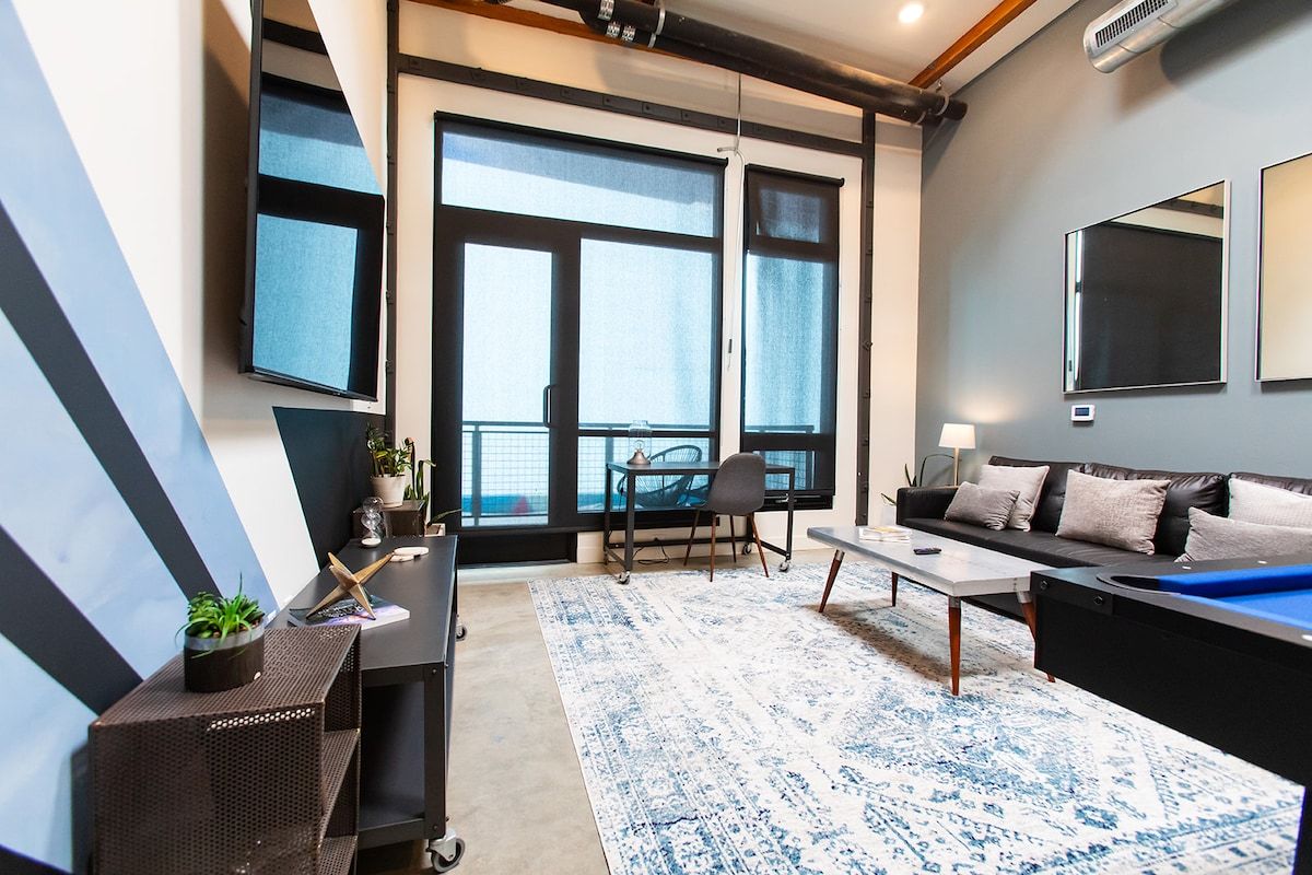 Un salon moderne avec un canapé, une table basse et une table à manger. Une grande fenêtre laisse entrer la lumière naturelle et offre une vue sur l’extérieur.