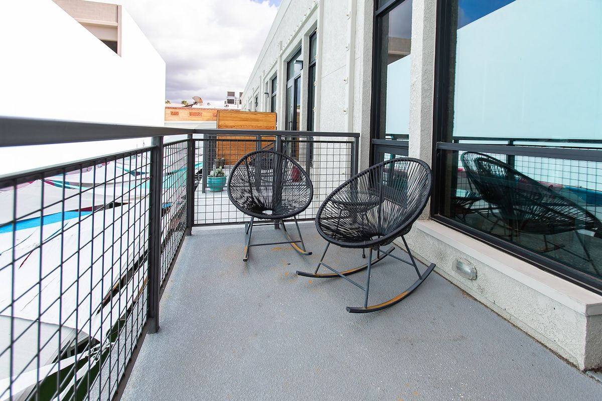 Un balcon avec deux fauteuils à bascule, une clôture en métal et une vue sur une piscine et des bâtiments en arrière-plan.