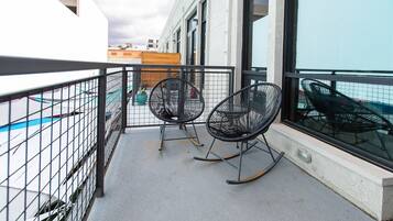 A balcony with two rocking chairs, a metal fence, and a view of a pool and buildings in the background.