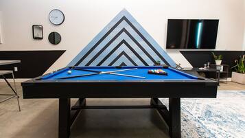 A pool table with a blue felt surface, surrounded by a geometric wall design.