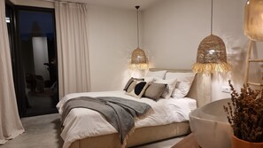 Une chambre moderne avec un grand lit, deux lampes suspendues, une table de chevet et une vue sur l’extérieur.