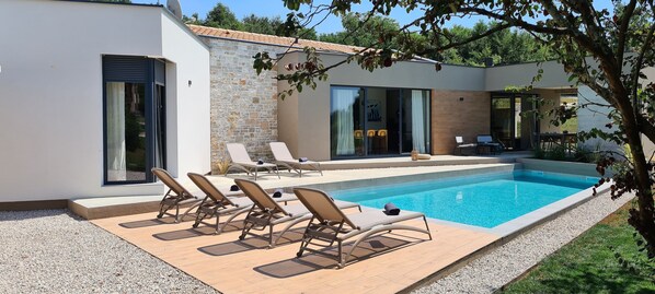 Un espace piscine extérieur moderne, doté de chaises longues et d’un mur en pierre.