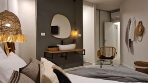 Une salle de bain moderne avec un miroir rond, un meuble-lavabo en bois, une chaise en osier et un lit agrémenté d’un tapis à motifs.