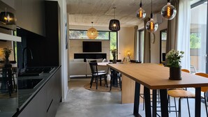 Une cuisine moderne avec une table à manger en bois, des chaises noires et des luminaires suspendus.