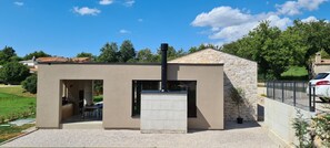 Une maison moderne avec une façade en pierre, un toit plat et un patio aménagé avec du mobilier d’extérieur.