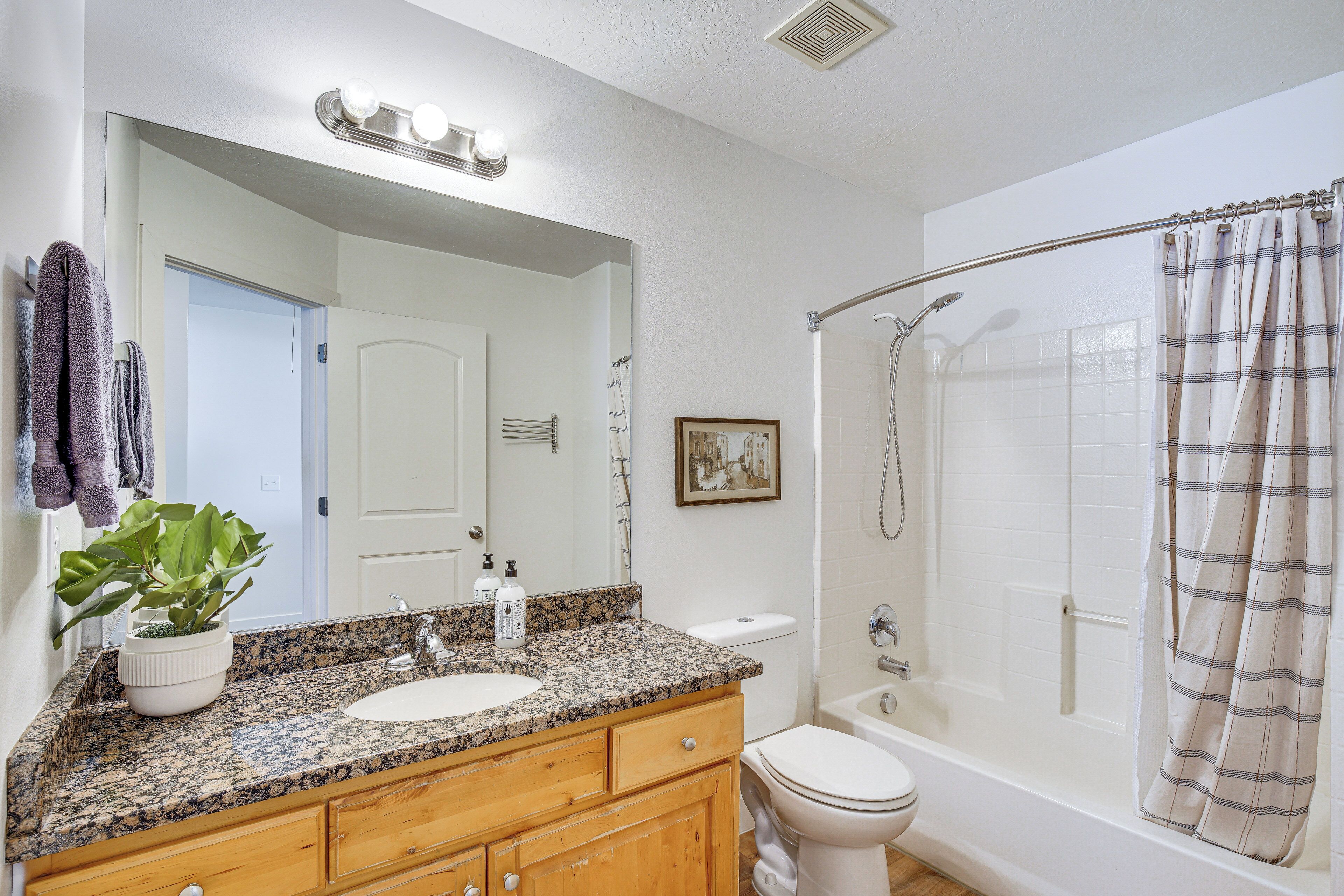 A bathroom with a granite countertop sink, wooden vanity, white toilet, and a walk-in shower with a curtain.