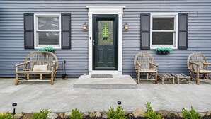 A house with a front porch, two wicker chairs, a small table, and a decorative door with a bear and tree design. - Peaceful Lake George Getaway - 3 Mi to Beach! (Lake George)