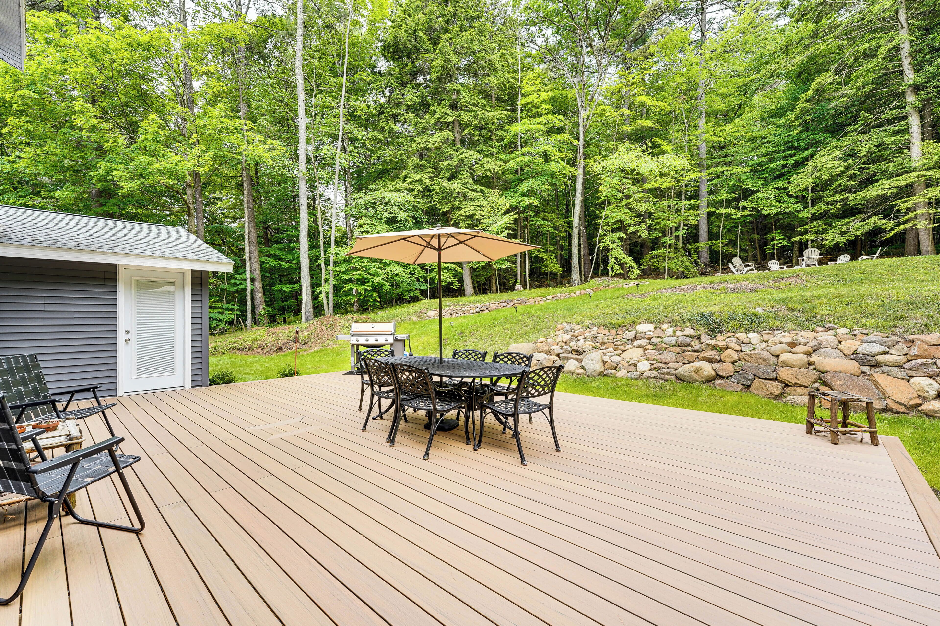 A wooden deck with a table and chairs, a barbecue grill, and a small shed.