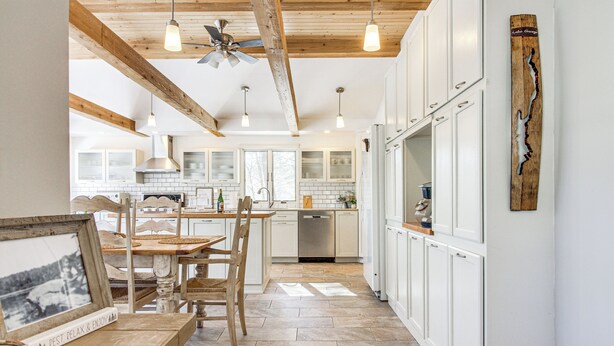 A kitchen with white cabinets, a wooden ceiling, and a dining area with a table and chairs. - Peaceful Lake George Getaway - 3 Mi to Beach! (Lake George)