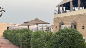 A rooftop terrace with neatly trimmed hedges, a building with scaffolding, and a clear sky. - VIP Al Fouad pyramids & spa (Giza)