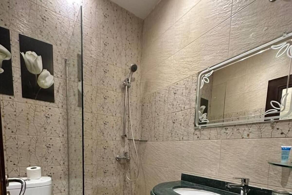 A bathroom with a glass-enclosed shower, a white toilet, a sink with a dark countertop, and a trash bin.