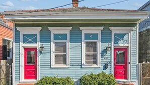 Una casa de dos pisos con puerta y ventanas rojas, número 443, con una chimenea de ladrillo y un pequeño porche delantero.