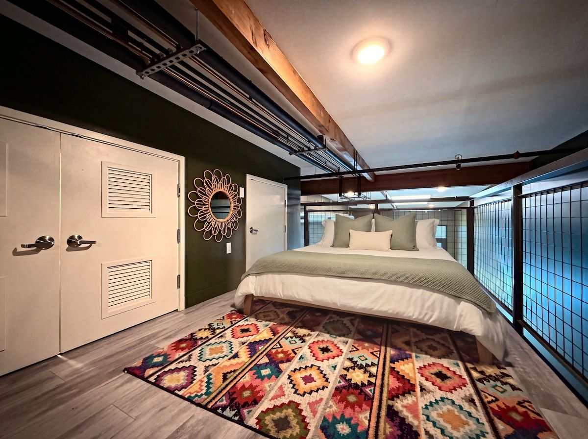 A bedroom with a bed, a patterned rug, a decorative wall piece, and a window with a view.