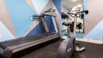 A gym with a treadmill, an elliptical, and a mirrored wall.
