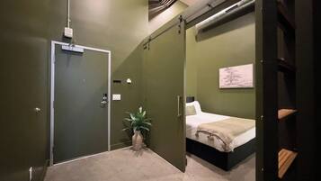 A room with a bed, a plant, and a door leading to another room.