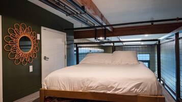 A bedroom with a bed, a colorful rug, a wooden ceiling beam, and a wall-mounted mirror.