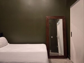 Een slaapkamer met een enkel bed, een houten deur en een spiegel.