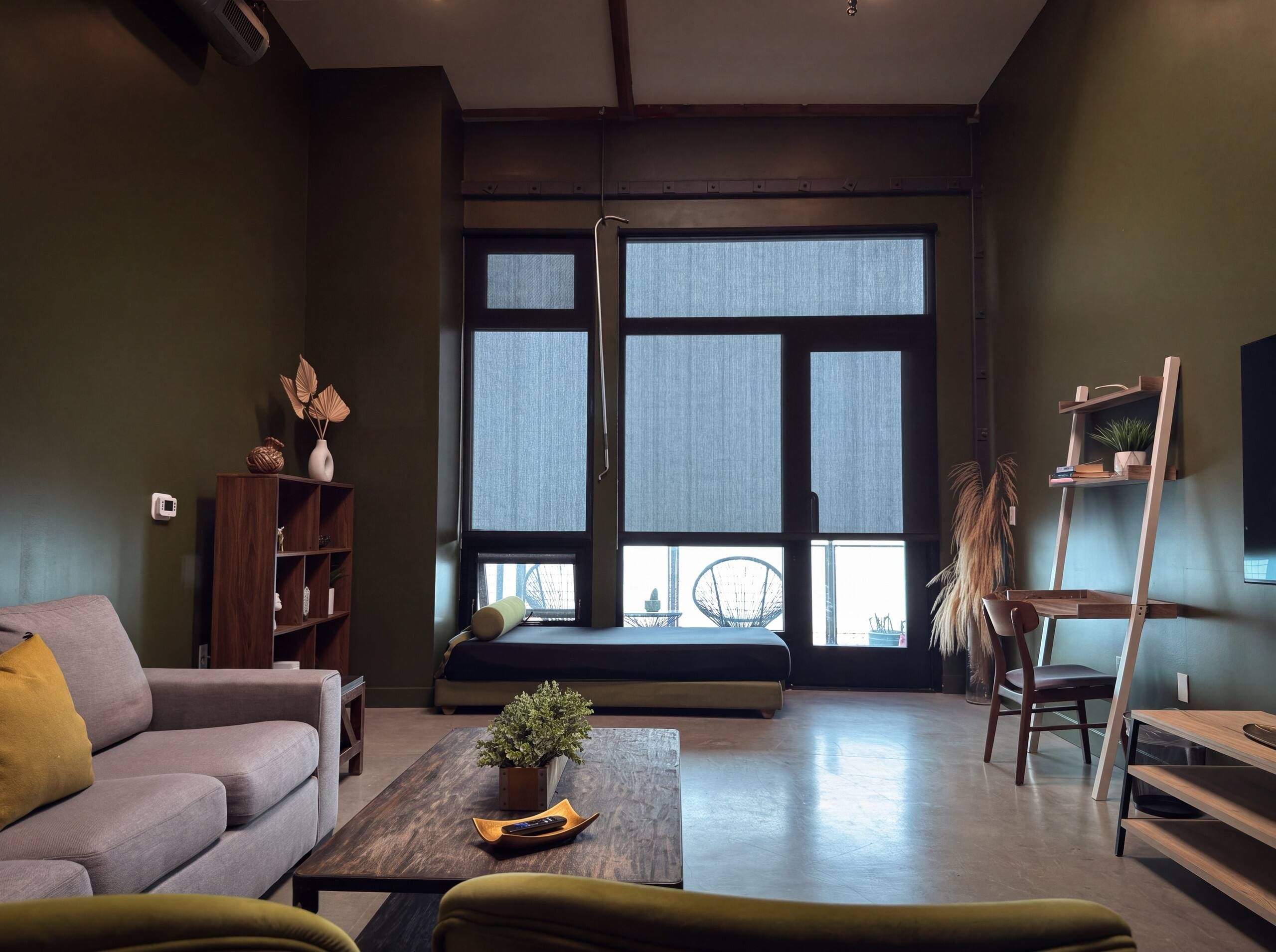 A modern living room with a sofa, a coffee table with a plant, a bookshelf, and a window with a view.
