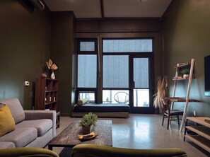 A modern living room with a sofa, a coffee table with a plant, a bookshelf, and a window with a view. - ⁂Pet Friendly⁂10min-Airport⁂AC⁂Gym⁂2Bed (Santa Ana)