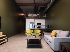 Een moderne woonruimte met een bank, twee fauteuils, een salontafel en een keuken op de achtergrond.