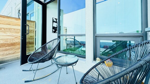 Een modern gebouw met grote glasramen, een houten wand en twee zwarte schommelstoelen ervoor.