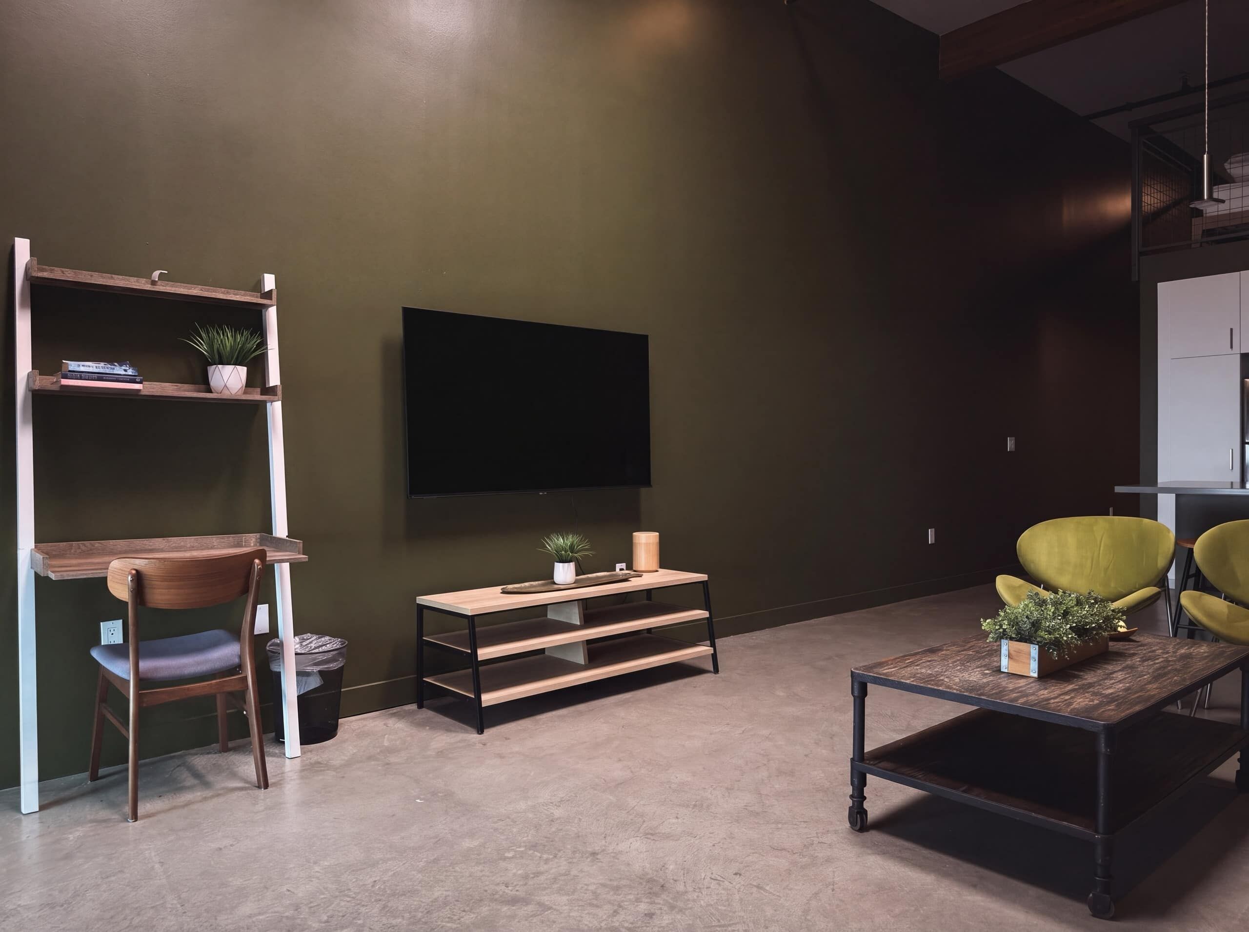 A modern living room with a flat-screen TV, wooden furniture, and a green accent wall.