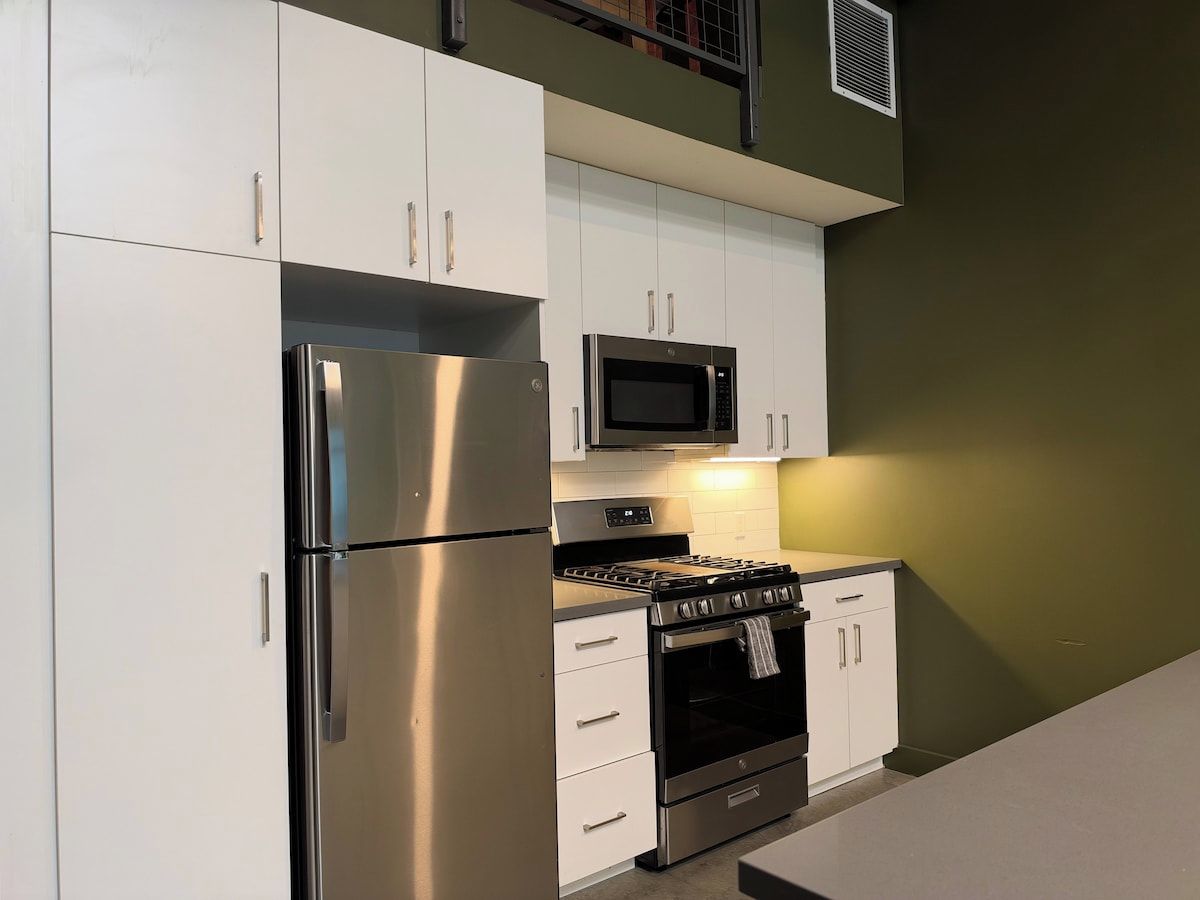 A kitchen with white cabinets, a stainless steel refrigerator, a microwave, and a stove.