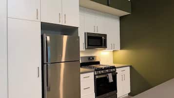 A kitchen with white cabinets, a stainless steel refrigerator, a microwave, and a stove.