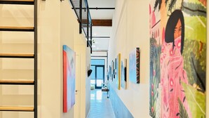 Een gang met kunstwerken aan de muur, een trap aan de linkerkant en een deur aan het einde.