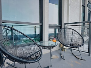 A balcony with two black wire-framed chairs and a small glass table.