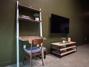 A room with a wooden chair, a small table, a shelf with books and a plant, and a TV mounted on the wall. - ⁂Pet Friendly⁂10min-Airport⁂AC⁂Gym⁂2Bed (Santa Ana)