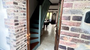 Ein schmaler Flur mit einer Treppe, die zu einer zweiten Etage führt, Backsteinwänden und einem gefliesten Boden.