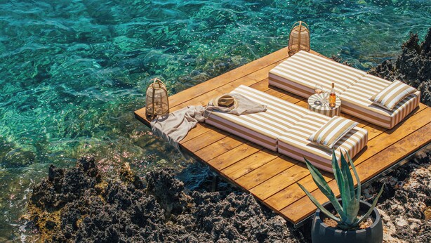 A wooden deck with two striped lounge beds, a lantern, and a bottle of wine. - Sewelo Suites (Zakynthos)