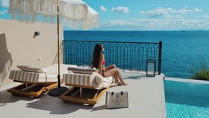 A woman relaxing on a sun lounger by a pool with a view of the ocean. - Sewelo Suites (Zakynthos)