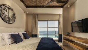 A hotel room with a large bed, a view of the ocean, a ceiling fan, and a mounted TV. - Sewelo Suites (Zakynthos)