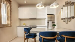 A modern kitchen with white cabinets, a marble countertop, and blue upholstered chairs. - Sewelo Suites (Zakynthos)