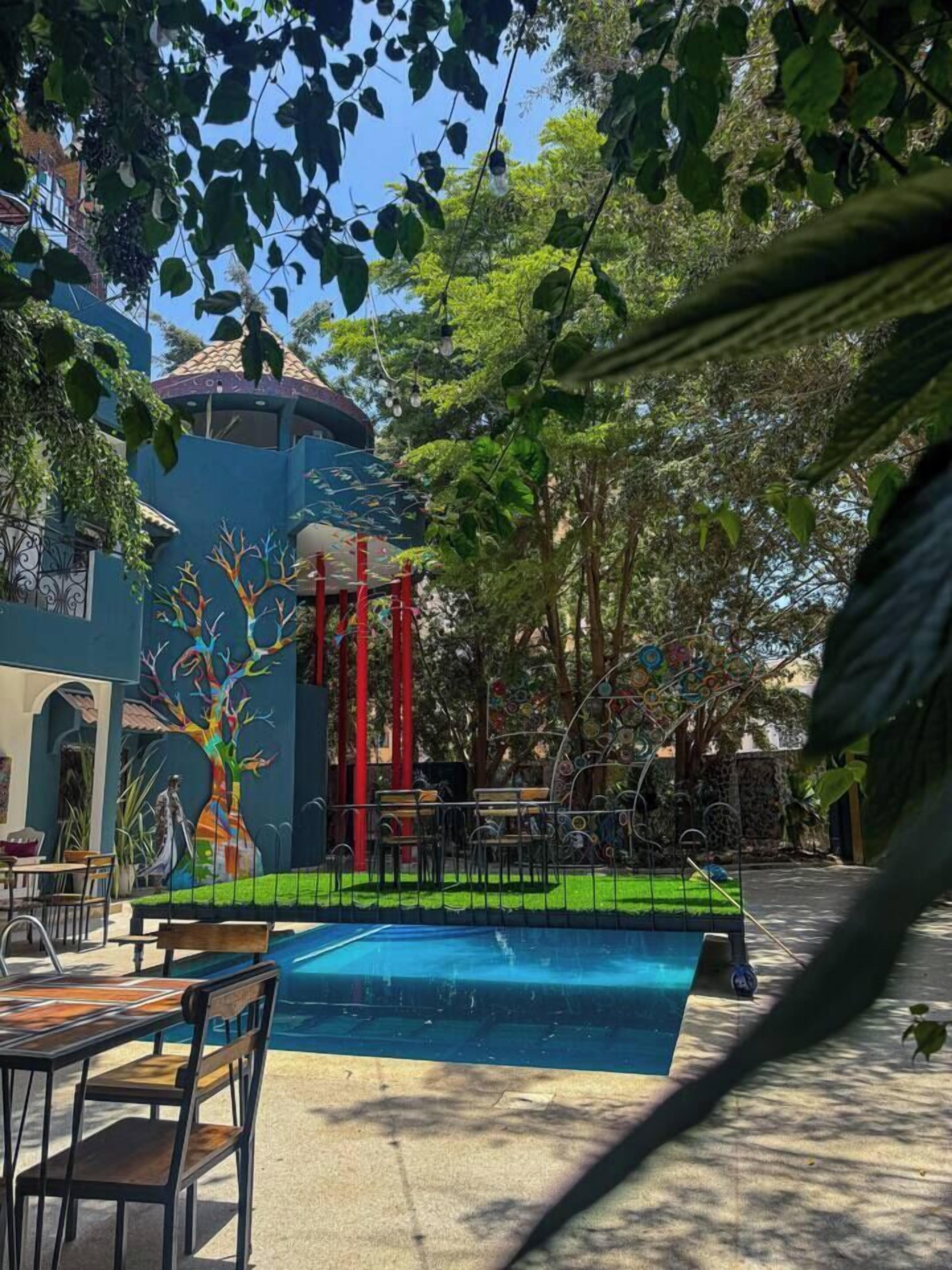 A pool area with a mural of a tree, surrounded by greenery and a building with a dome.