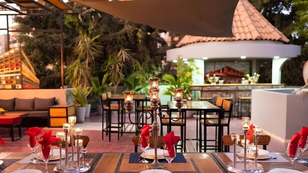 An outdoor dining area with tables set for two, featuring candle centerpieces and red napkins.