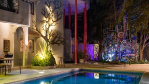 A swimming pool with a tree sculpture, red pillars, and a colorful wall art installation.