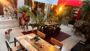 An indoor dining area with wooden tables and chairs, potted plants, and a decorative wall.