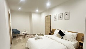 Ein modernes Schlafzimmer mit einem großen Bett, einem Nachttisch, einem Sessel und einem kleinen Tisch mit einer Lampe.