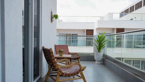 Ein Balkon mit Holzstuhl und Tisch, Blumentöpfen und Blick auf die Außenansicht des Gebäudes.