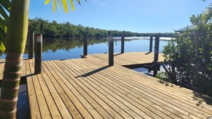 A wooden dock extending into calm water, surrounded by lush greenery and a clear sky. - The Everglades House (Ochopee)