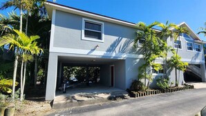 A two-story house with a garage, surrounded by palm trees and a clear blue sky. - The Everglades House (Ochopee)