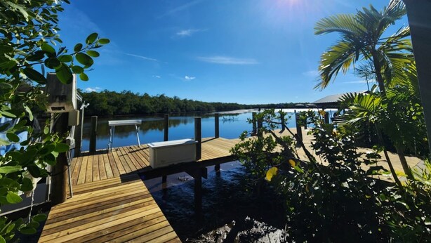 A wooden deck with a view of a calm lake and a forested shoreline. - The Everglades House (Ochopee)