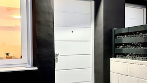 Une porte moderne avec une fenêtre au-dessus, un paillasson sur lequel est écrit le mot « VACANCES », et un mur de briques.