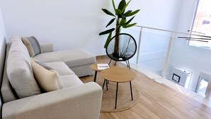 Un salon moderne avec un canapé beige, une table basse ronde en bois, une chaise à armature métallique noire et une grande plante verte.